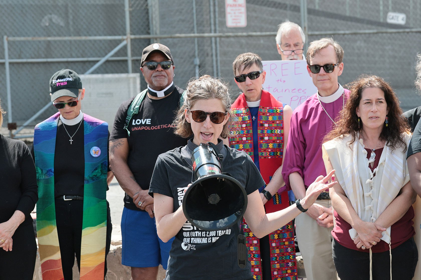 A group of faith leaders standing together. The person in front is holding a megaphone.