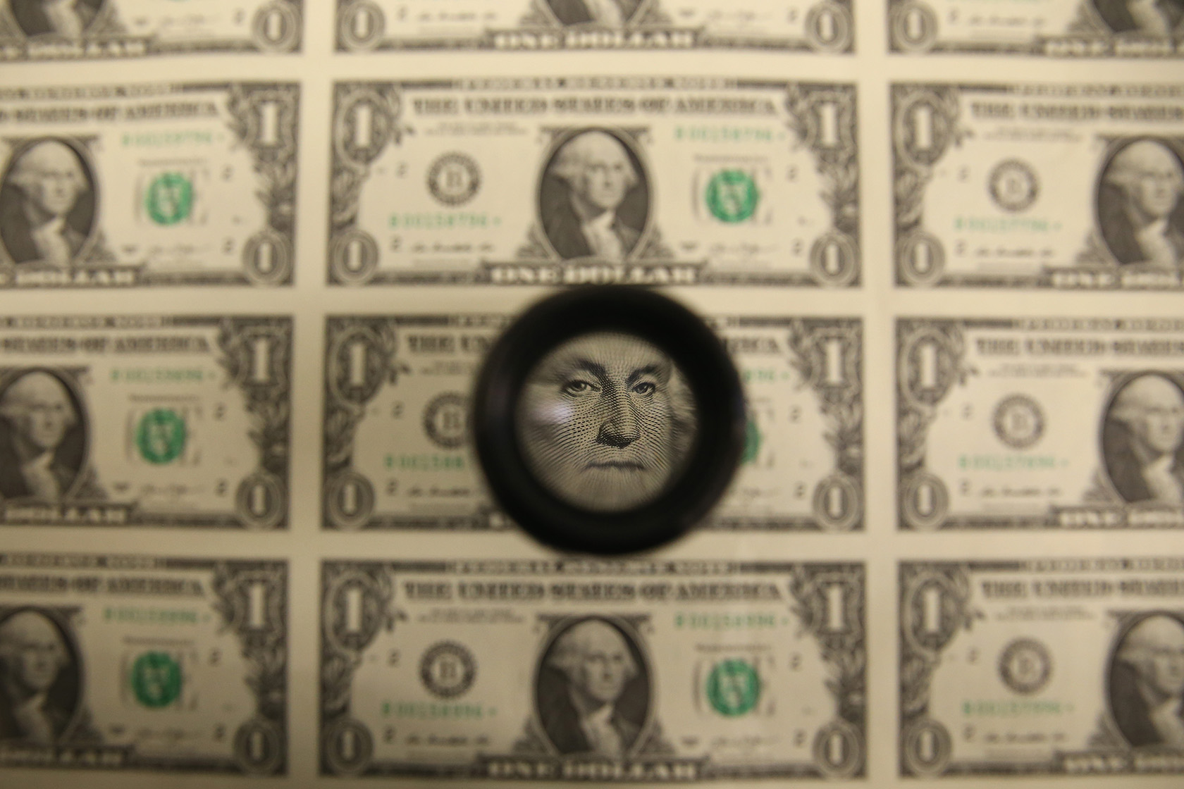 A magnifying glass is used to inspect newly printed $1 bills.