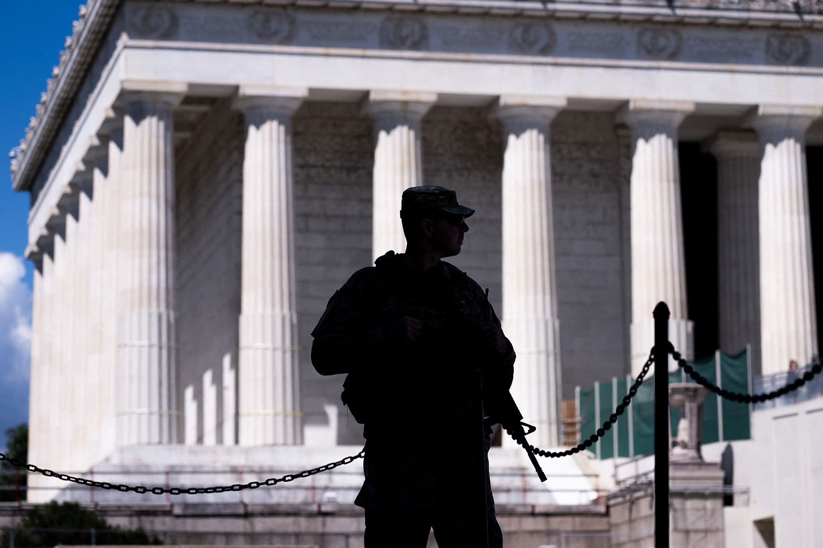 Armed National Guard member foregrounded in silhouette in front of pillars of Lincoln Memorial